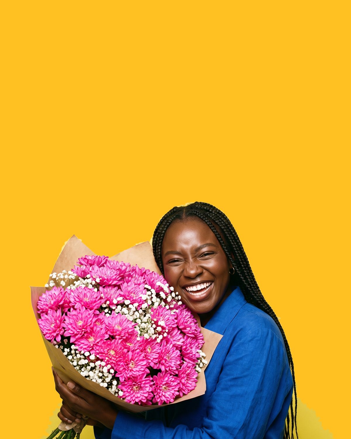 A woman laughing with a dense bouquet of hot-pink chrysanthemums held up against her cheek
