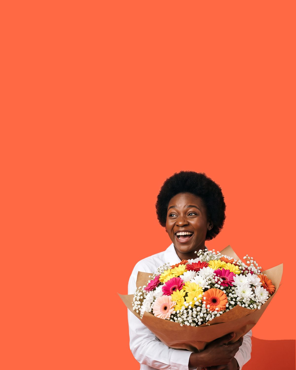 A woman caught mid-laugh in surprise, holding a bright mixed gerbera daisy bouquet at chest height