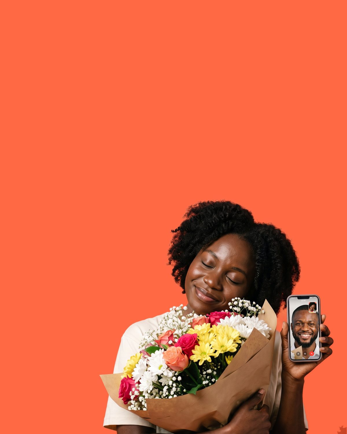 A woman hugging a bouquet of mixed fresh flowers with her eyes closed, holding up a phone with a man smiling back from the video call on its screen