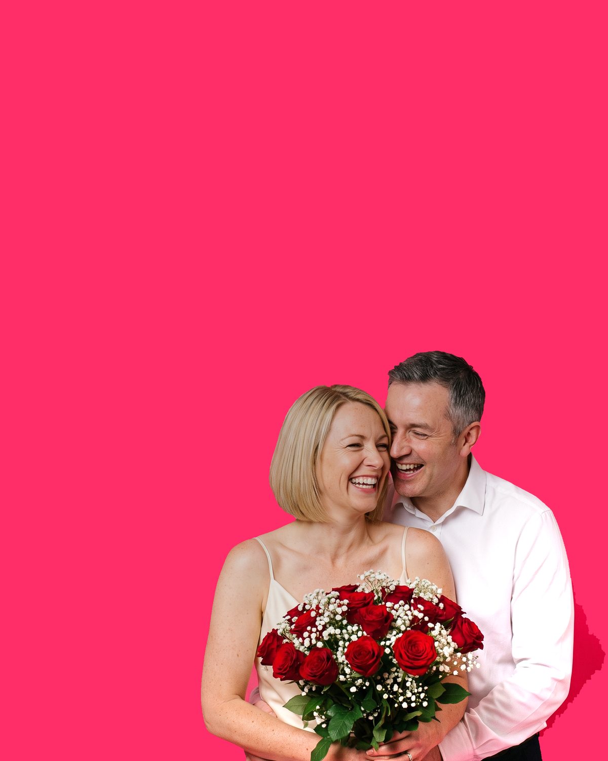 A couple cheek to cheek, a blonde woman laughing while a grey-haired man holds her, a bouquet of red roses and gypsophila in her arms