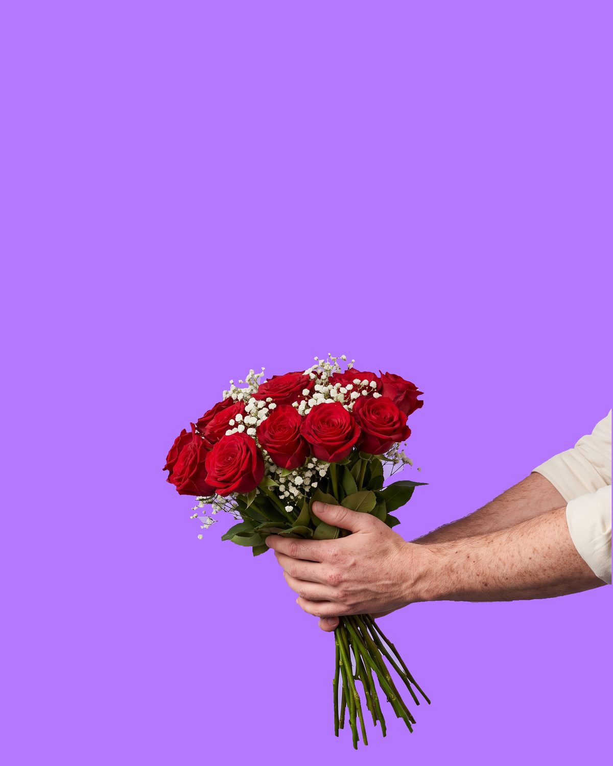 An outstretched arm in a cream sleeve offering a bunch of red roses and gypsophila, held out to the viewer