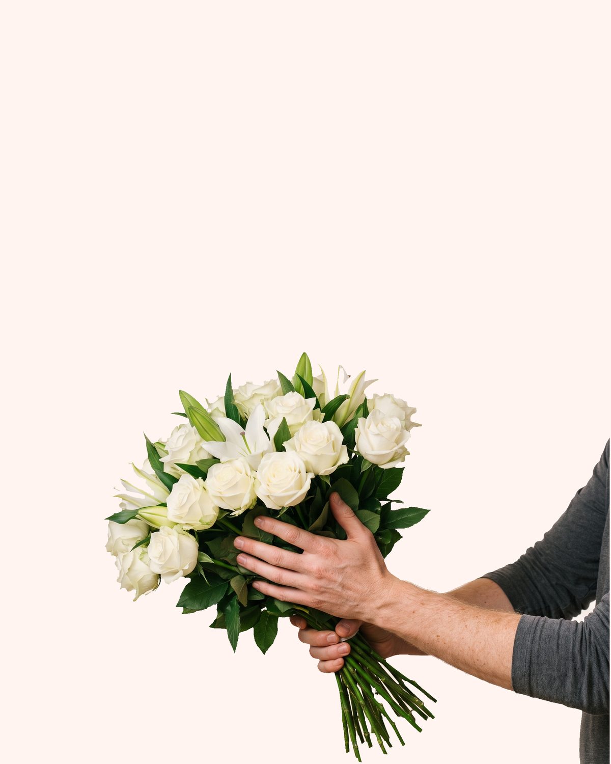 A hand in a dark sleeve holding out a quiet bouquet of white roses and lilies