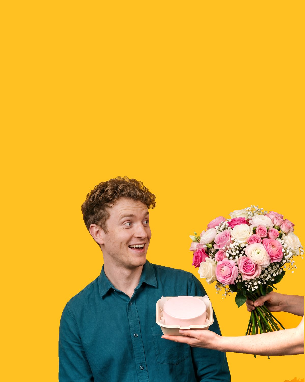 A red-haired man in a blue shirt caught mid-surprise as a bouquet of pink roses and a pink cake box are held out to him