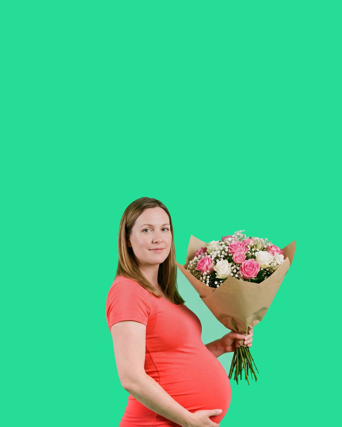 A pregnant woman in a coral dress standing side-on, her bump clearly showing, holding a wrapped bouquet of pink and white roses